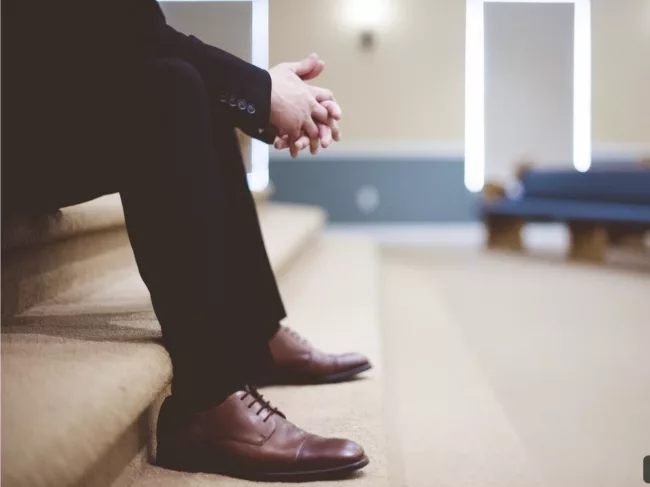Homme assis sur un escalier, en tenue formelle, incarnant une posture humble et réfléchie, symbole de leadership conscient et d’introspection managériale.