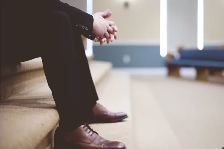 Homme assis sur un escalier, en tenue formelle, incarnant une posture humble et réfléchie, symbole de leadership conscient et d’introspection managériale.